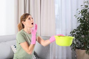 Woman catching water in leaky ceiling