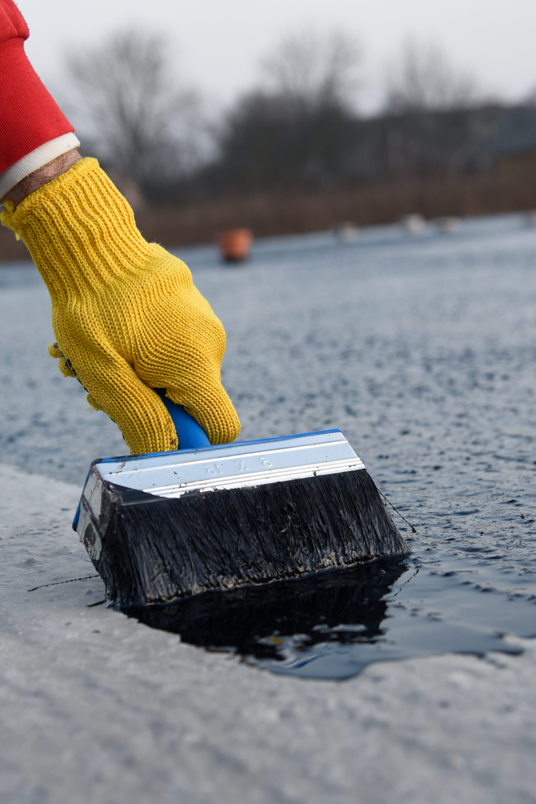 Roofer worker painting bitumen praimer at concrete surface by the roller brush. Waterproofing. Waterproofing foundation building. Roof coating