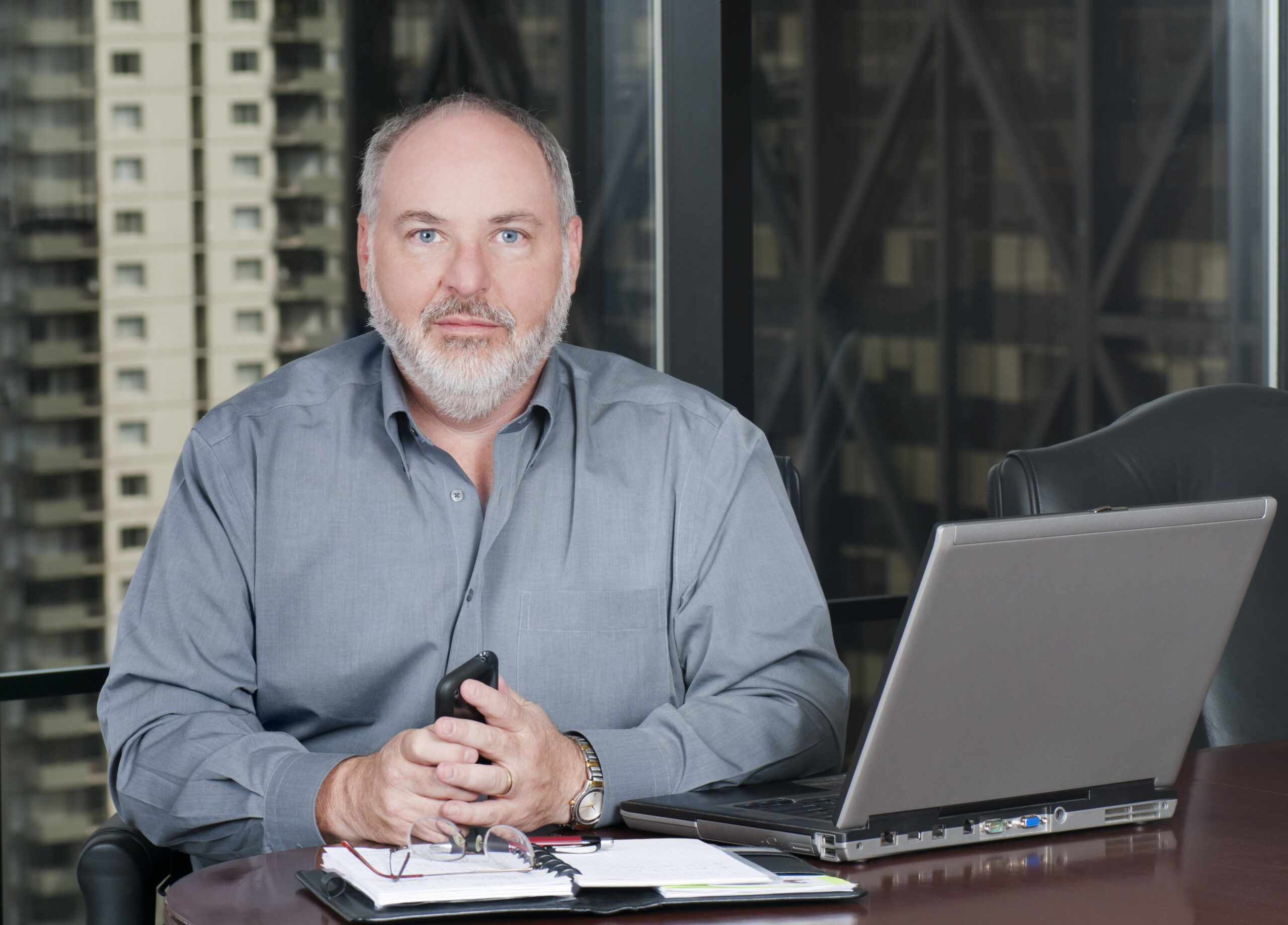 "A businessman at a table with his laptop and notebook, looking at the camera.  Blurred background is the view out of this 20th floor office window.For more of this model, plus my other Business related shots, click below:"