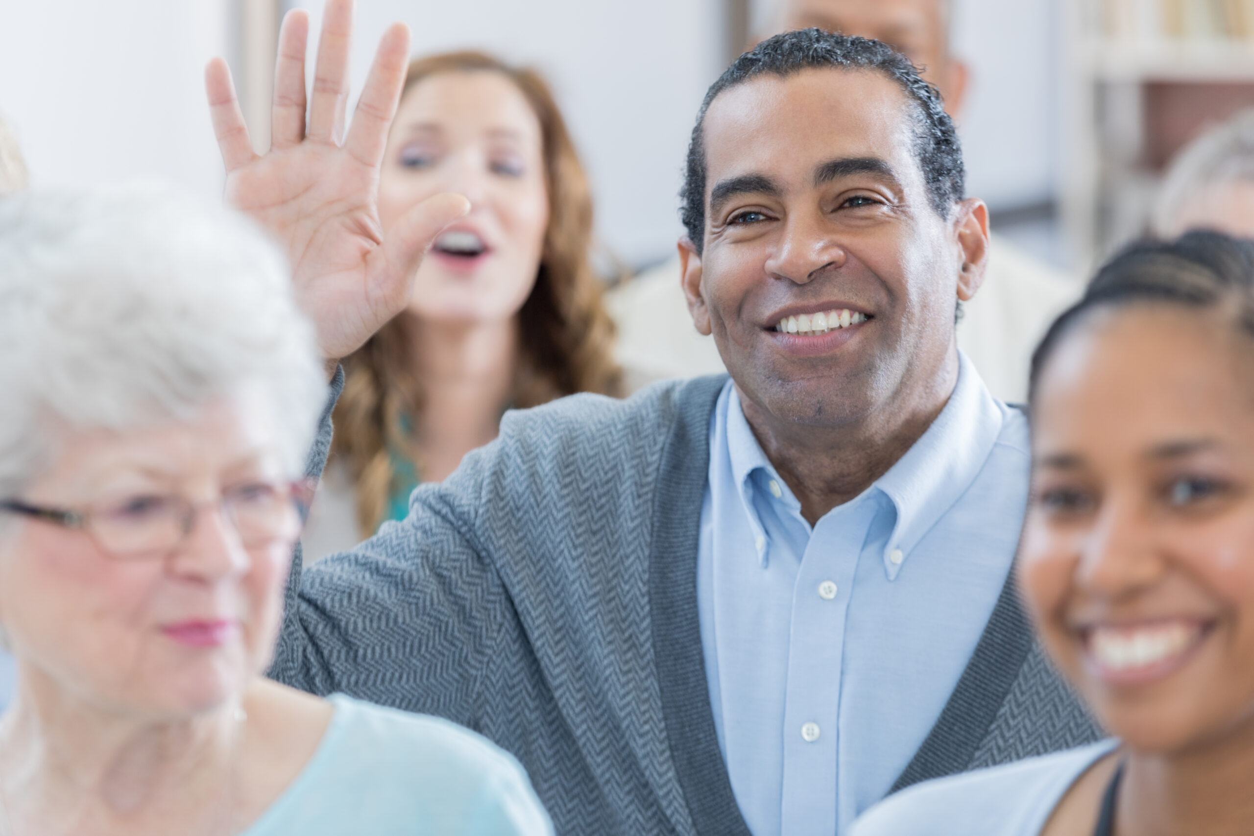 Handsome senior African American businessman raises his hand to ask a question during a seminar or conference. He is sitting with a group of his colleagues.