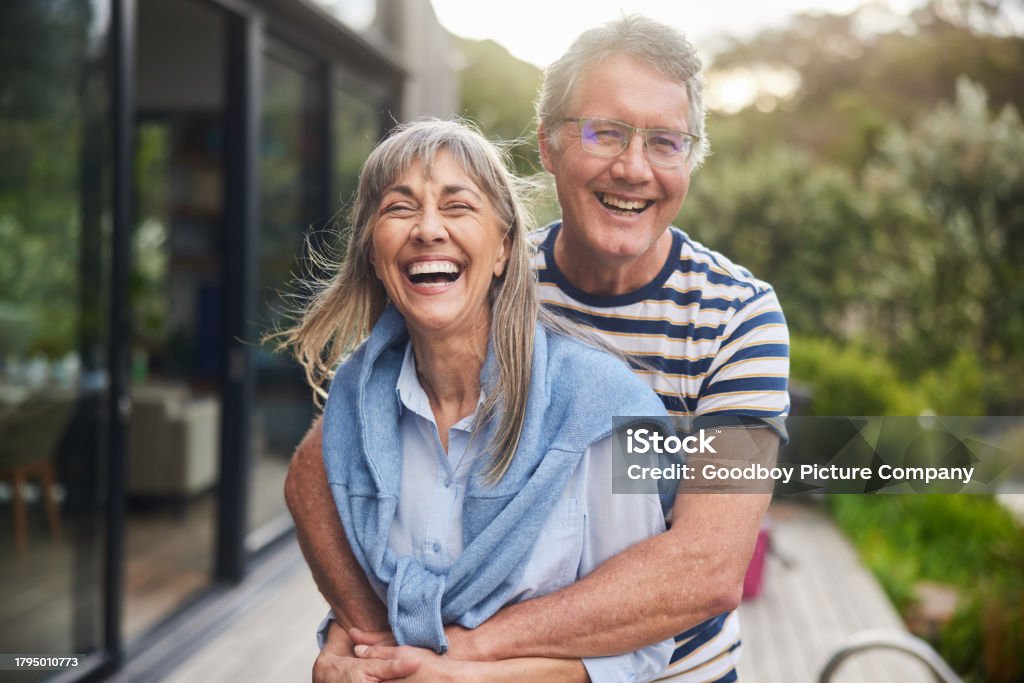 Mature couple standing arm in arm together and laughing outside in the back yard at home in summer