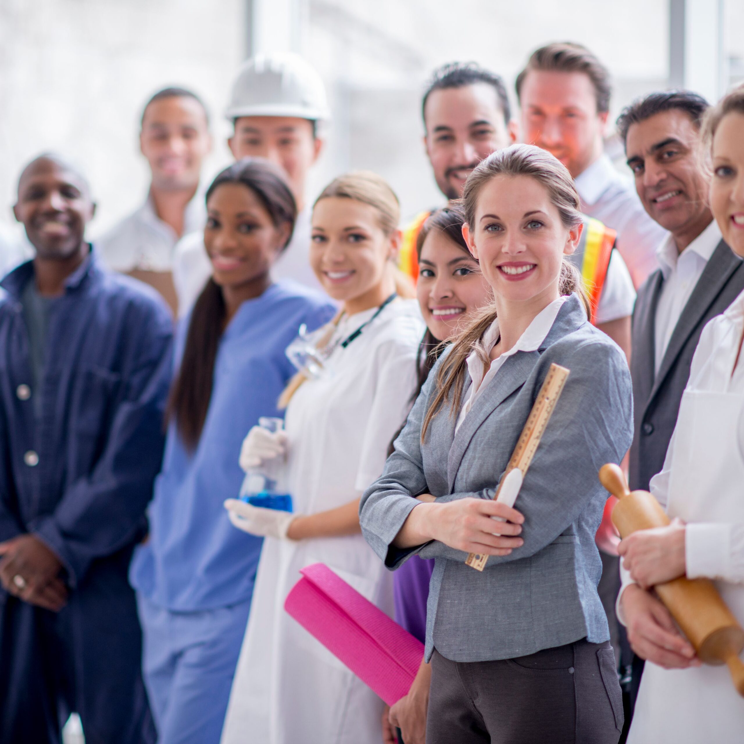 A multi-ethnic group of varied business professionals are standing together and are smiling while looking at the camera.