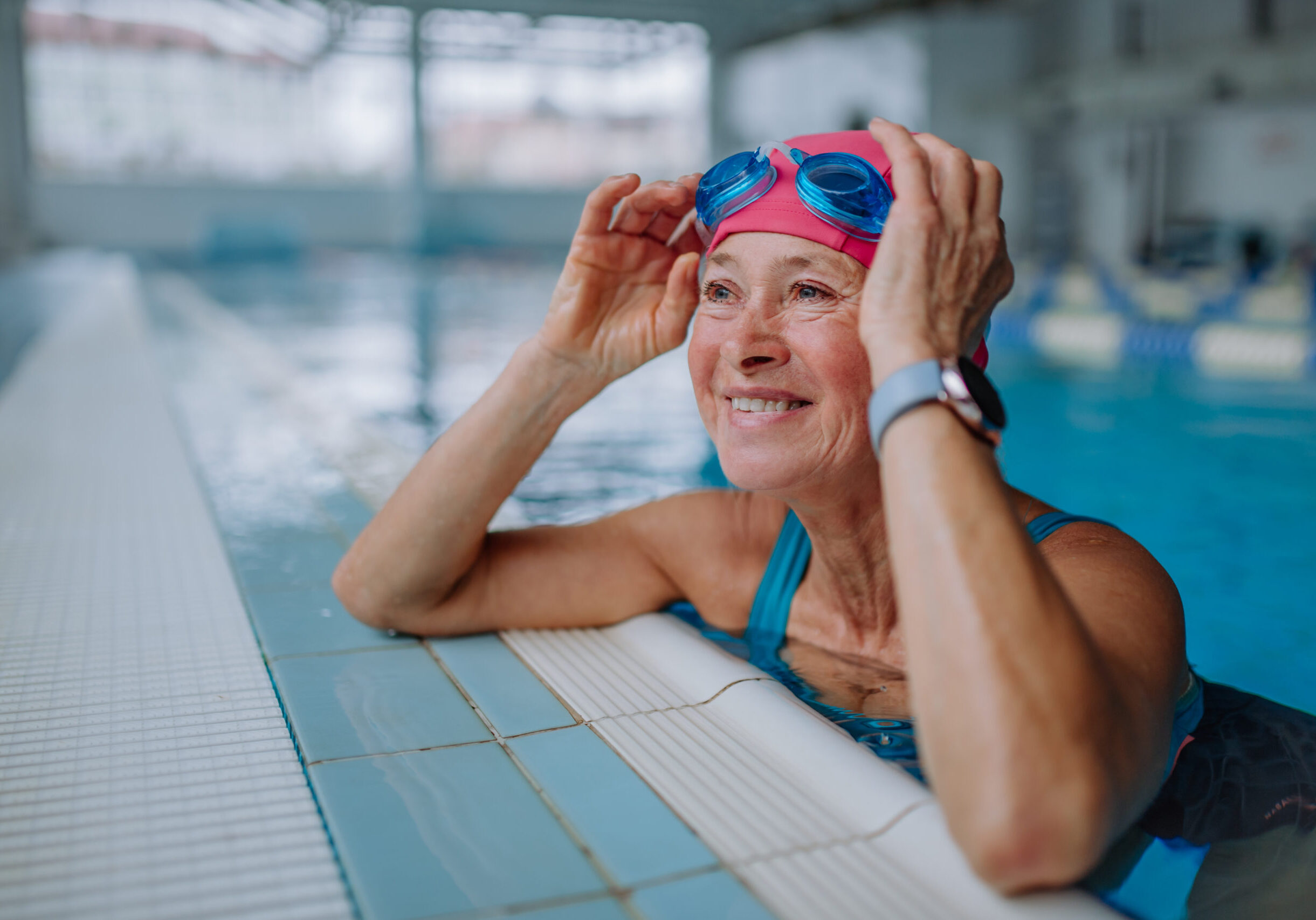 Happy senior woman in swimming pool, leaning on edge.