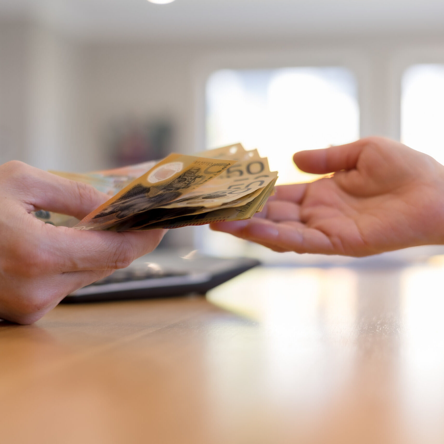 Close-up of hands exchanging Australian dollar banknotes across desk. Concept of cash payment, money transaction, financial exchange, business deal personal finance in everyday context.